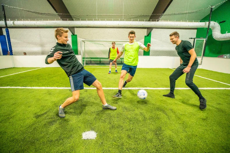 drei junge Männer spielen in einer Indoor Arena Fußball